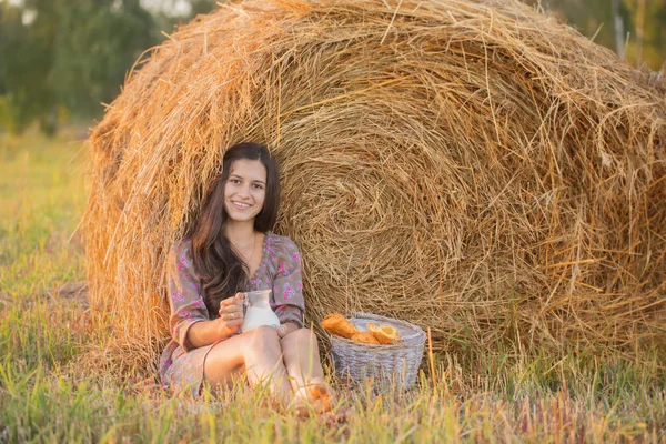 A smiling girl in a field of haystacks with a jug of milk