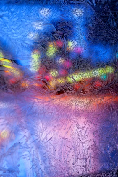 Multicolored lights of the city behind frosty glass with frosty patterns