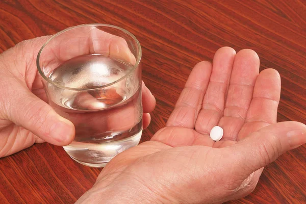 One tablet and glass with water in hands