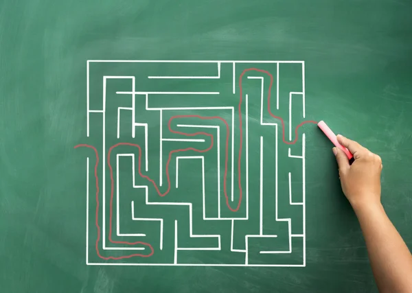 Hand solving maze drawn on blackboard