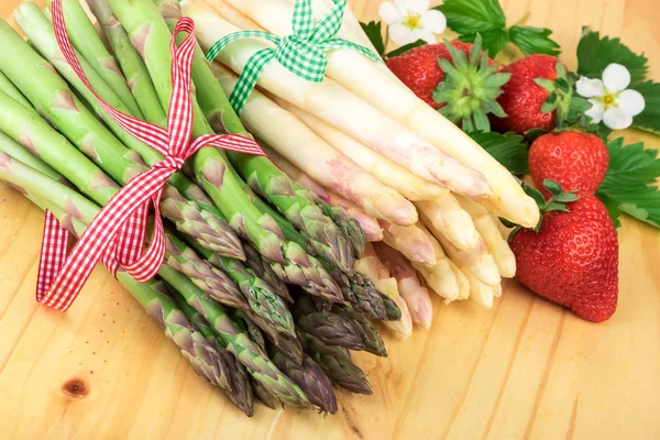 Green white asparagus with fresh strawberries on bright wood. Healthy cooking concept.