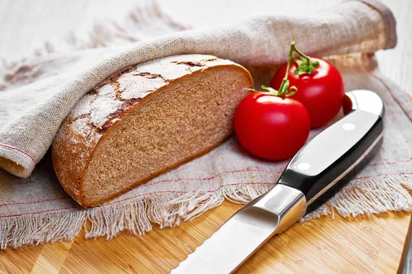 Sliced loaf of gray floured bread, tomatoes and knife