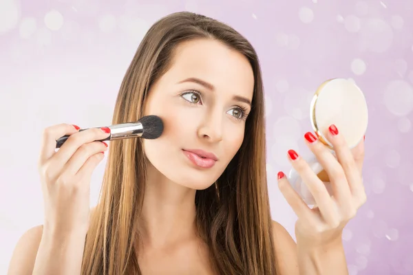 Woman holding  a mirror and applying  makeup