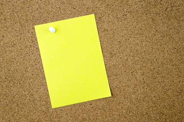 Blank yellow paper note pinned on cork board