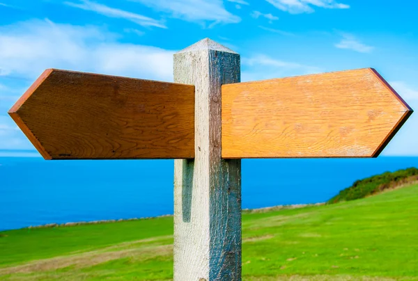 Blank wooden signpost with two arrows over clear blue sky with copy space