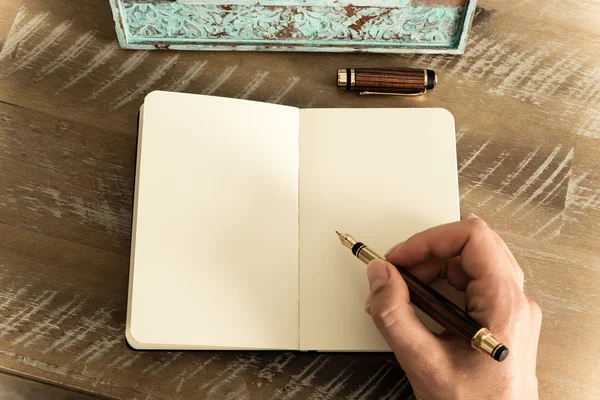 Retro effect and toned image of a woman hand writing a note with a fountain pen on a notebook.