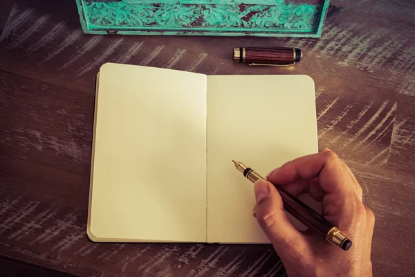 Retro effect and toned image of a woman hand writing a note with a fountain pen on a notebook.