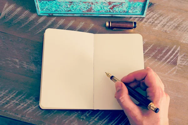 Retro effect and toned image of a woman hand writing a note with a fountain pen on a notebook.