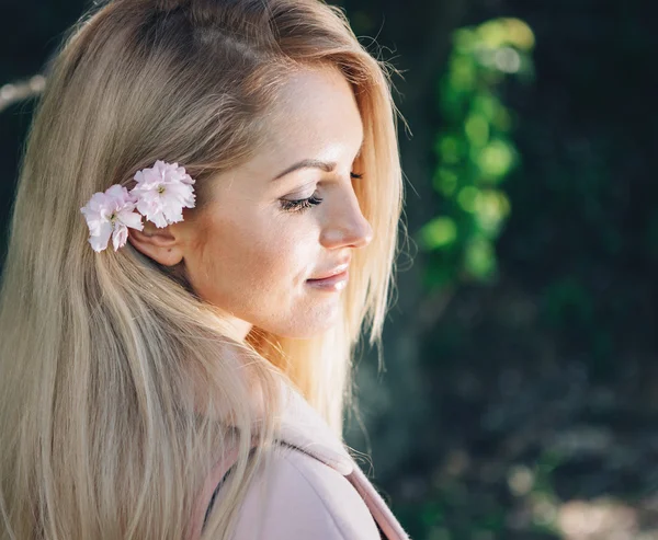 Woman with  long blond hair in the garden with flowers. Beautiful girl on a sunny day.