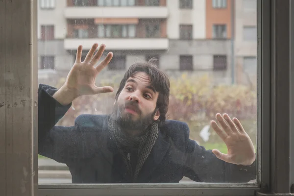 Young handsome bearded man posing behind a glass