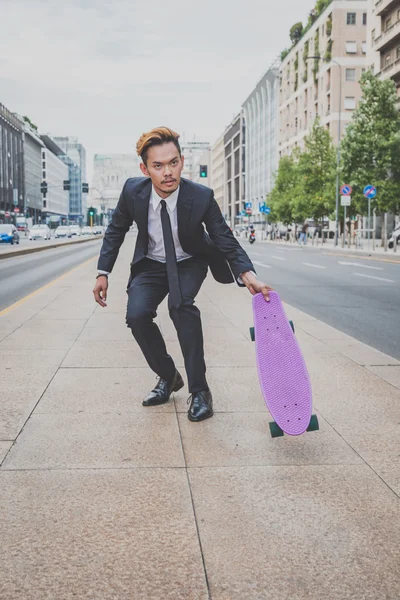 Young handsome Asian model posing with his skateboard