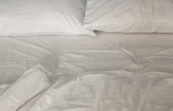 An unmade bed with white linens