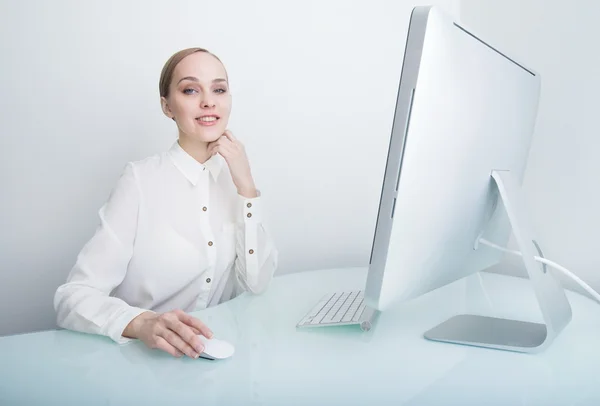 Attractive smiling young business woman working on computer in the office at the desk looking at the camera