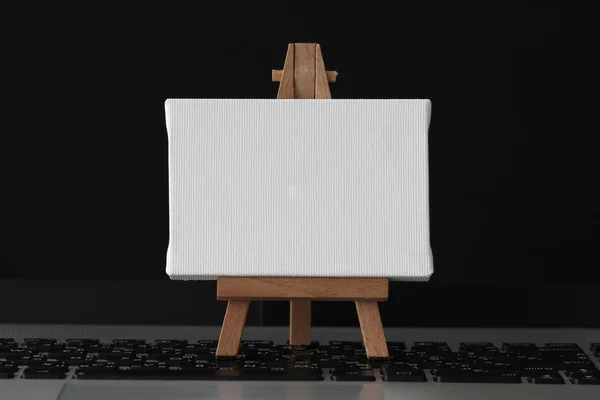 Blank canvas and wooden easel on laptop computer as concept