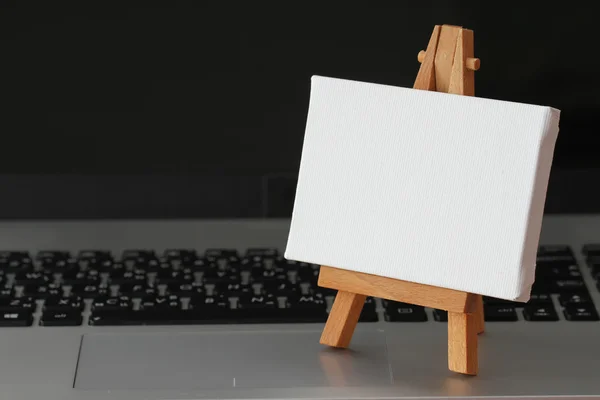 Blank canvas and wooden easel on laptop computer as concept