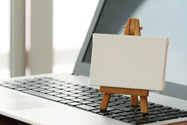 Blank canvas and wooden easel on laptop computer as concept