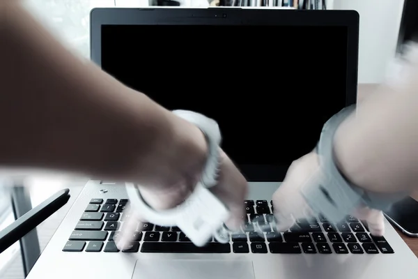 Businessman hand in handcuffs at wooden desk with laptop compute