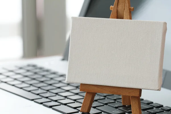 Blank canvas and wooden easel on laptop computer as concept
