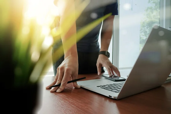 Designer hand working laptop with green plant foreground on wood