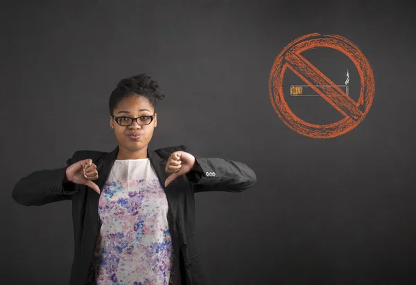 South African or African American black woman teacher or student with thumbs down hand signal to no smoking on a chalk black board background inside