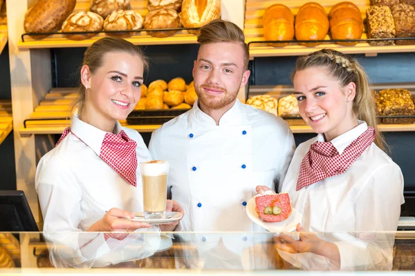 Baker and shopkeepers in bakery posing and presenting coffee and sandwiches