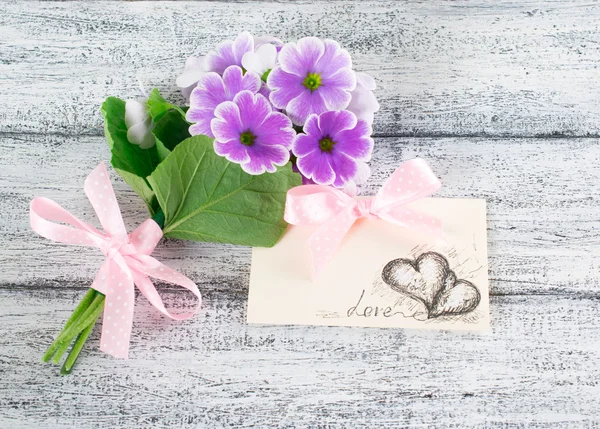 Bouquet of violet primroses and paper greeting card with hearts
