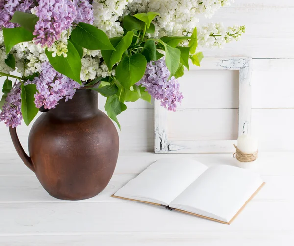 Lilac bouquet in clay jug with open book and candle in rustic st