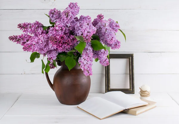 Lilac bouquet in clay jug with open book and candle in rustic st