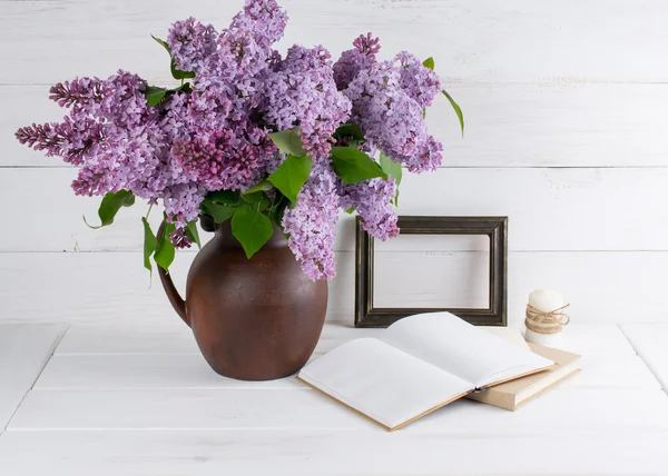 Lilac bouquet in clay jug with open book and candle in rustic st