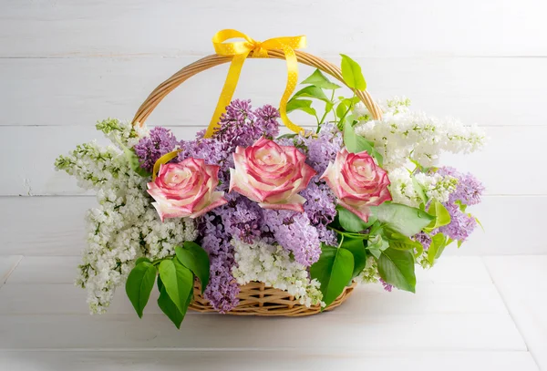 Lilac bouquet with roses in basket on background of shabby woode