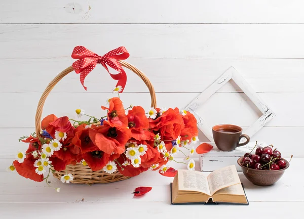 Daisy and poppies bouquet in basket with open book and tea