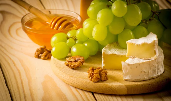 Still life of cheese, honey, walnuts and grapes