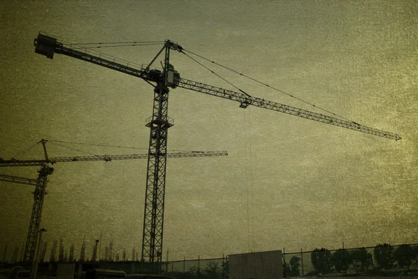 Industrial construction cranes and building silhouettes over sun