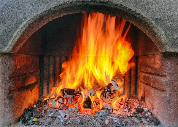 Outdoor brick fireplace with a fire blazing inside.