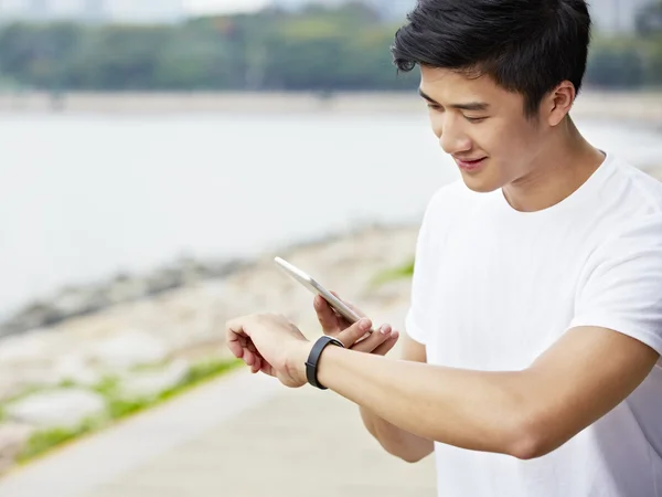 Young asian man checking cellphone and watch before exercise