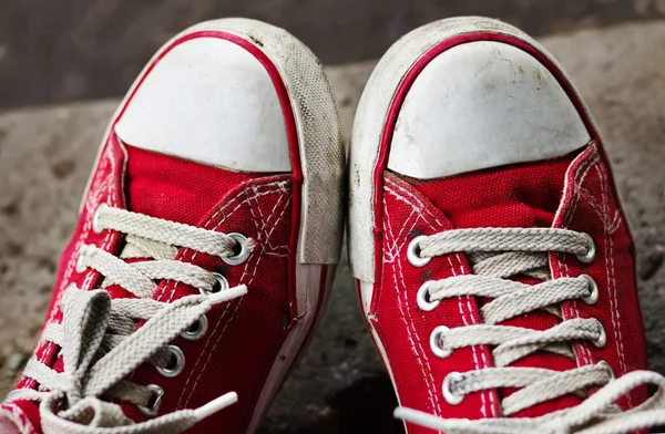 Feet in dirty red sneakers and jeans outdoors.