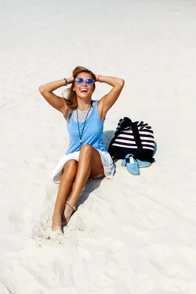 Woman in sunglasses with backpack and shoes on sand