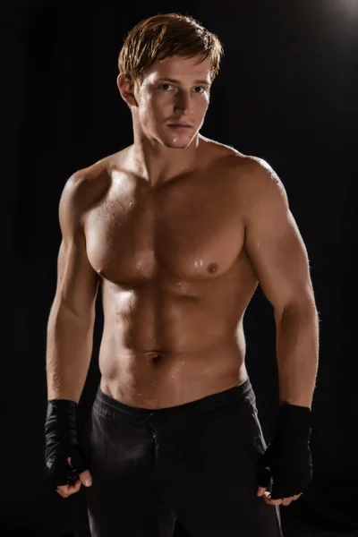 Side view of muscular man boxing on black background