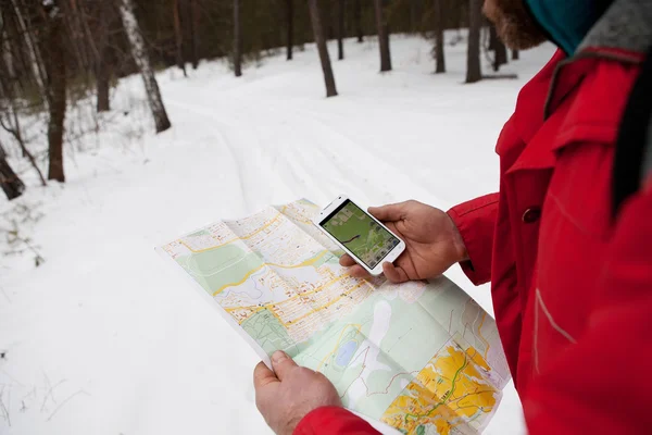 Phone and map in the hands of men hiking winter forest