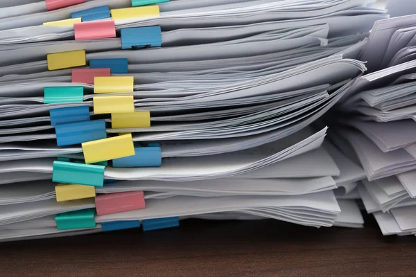 Two piles of documents with colorful clips on desk stack up