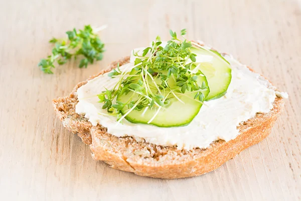 A slice of bread topped with cream cheese, cucumber and watercress