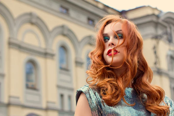 Art Photo.Attractive red-haired girl, red lips and green eyes, walks through the city, the wind fluttering hair. Walk near Kiev Opera House. Image toned and noise added