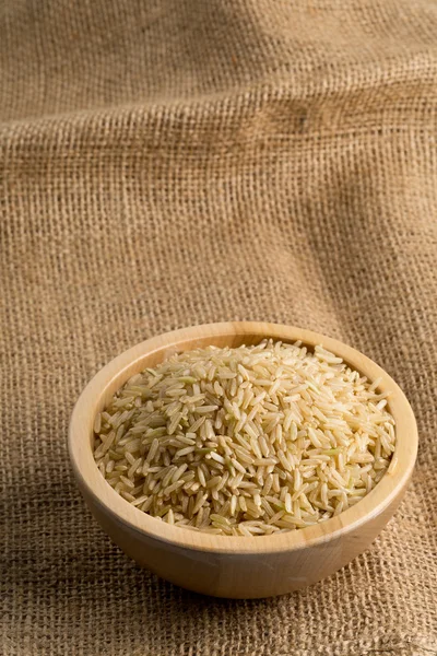 Natural brown uncooked rice in wooden bowl on burlap