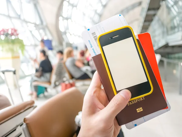 Hand holding passport, boarding pass and smart phone in airport