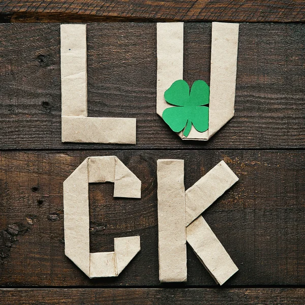 Craft paper origami LUCK lettering on dark barn wood rusctic background. Green clover leaf. St. Patrick\'s Day greeting postcard template.