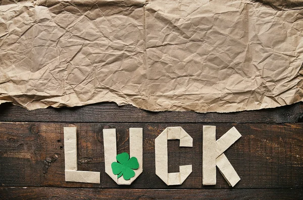 Craft paper origami LUCK lettering on dark barn wood rusctic background. Green clover leaf. St. Patrick\'s Day greeting postcard template. Space for copy, text, lettering.