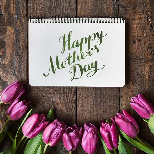 Hapy Mother\'s Day brush nib lettering calligraphy. Pink, tulips bunch on dark barn wood planks background. Postcard template.