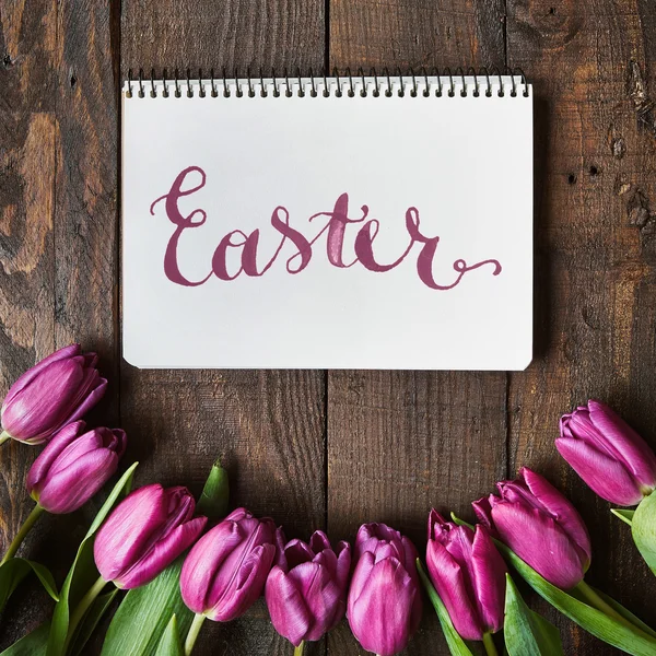 Easter brush nib lettering calligraphy. Pink, tulips bunch on dark barn wood planks background. Postcard template.