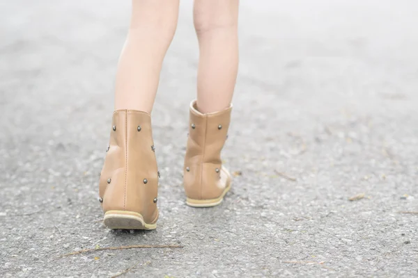 Little girl legs with boot on asphalt road