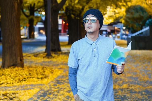 An asian man in a polo t-shirt walks in a street in autumn